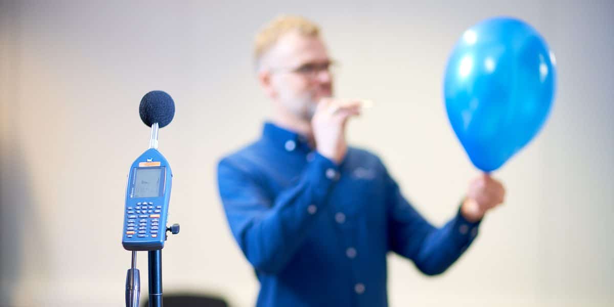 En støymåler foran mann med blå ballong
