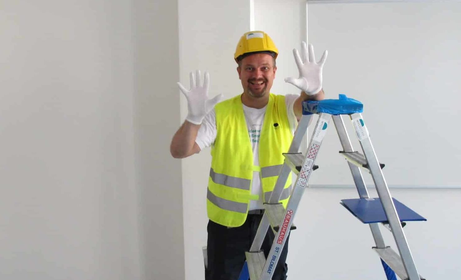 Smilende mann i gul vest viser hender med rene hvite hansker
